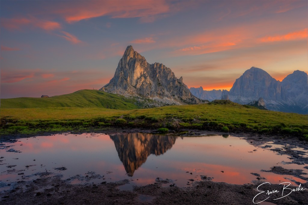 Dolomites peaks and glowing dawn clouds reflected in still mountain water.